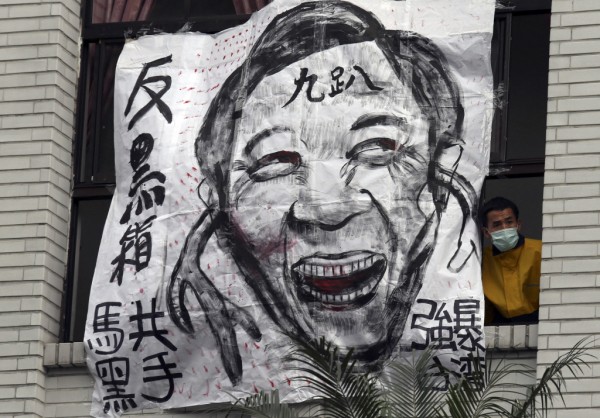A protester looks out from a window next to a cartoon depicting Taiwan's President Ma Ying-jeou at Taiwan's legislature in Taipei