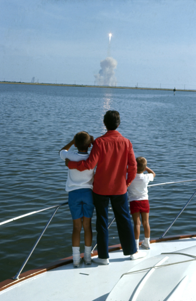Jan Armstrong, wife of Apollo 11 astronaut Neil Armstrong, gazing upon white trail in sky of Apollo 11 blastoff, from boat, with son. Photo: TIME.
