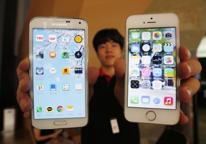 A sales assistant holding Samsung Electronics' Galaxy 5 smartphone (L) and Apple Inc's iPhone 5 smartphone (R) poses for photographs at a store in Seoul July 16, 2014. REUTERS/KIM HONG-JI