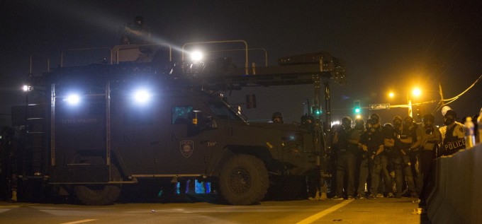 Police officers keep watch while demonstrators protest the death of black teenager Michael Brown in Ferguson